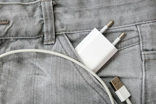 Cargador USB, enchufe de cable y adaptador en bolsillo gris vaqueros, no se olvide del cargador en casa — Foto de Stock