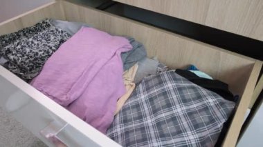 Kadın elleri elbiseleri çekmeceye koyuyor, düzenliyor, katlıyor ve daktilo ediyor.