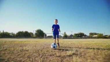 Çocuk topa vuruyor. Çocuk büyük bir futbol sahasında top sürmek için antrenman yapıyor. Futbol konsepti. Futbolcu topu kaleye atıyor. Fakir bir bölgede sokak sporları. Çocukluk