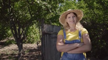 Genç kadın çiftçi çiftlikte duruyor. Tarım. Bahçedeki bir kadın bahçıvanın portresi. Küçük bir aile şirketi. Güneşli bir günde hasır şapka takan bir tarım işçisi. Organik tarım ve sağlıklı beslenme