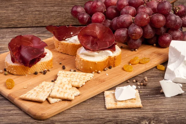 Queijo branco, presunto e uva em prato de madeira — Fotografia de Stock