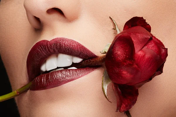 Kobieta z czerwona szminka gospodarstwa czerwoną różę w usta — Zdjęcie stockowe