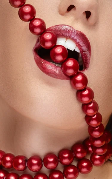 Mouth with red lipstick biting red pearls — Stock Photo, Image