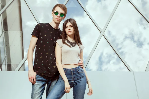 Gorgeous young couple posing in jeans in front of office glased — Stock Photo, Image