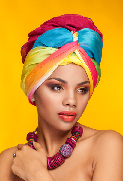 Afro american girl wearing an ethnic turban on yellow background in studio photo. Beauty and culture