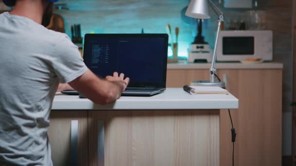 Мужчина-хакер печатает на клавиатуре в наушниках, работает из дома — стоковое видео