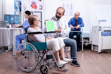 Rehabilitasyon merkezinde yeşil ekran tableti olan doktor.