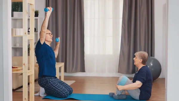 Active grandma using resistance band sitting on yoga mat at home
