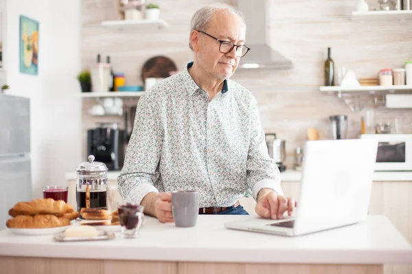 Senior man using laptop in the kitchen