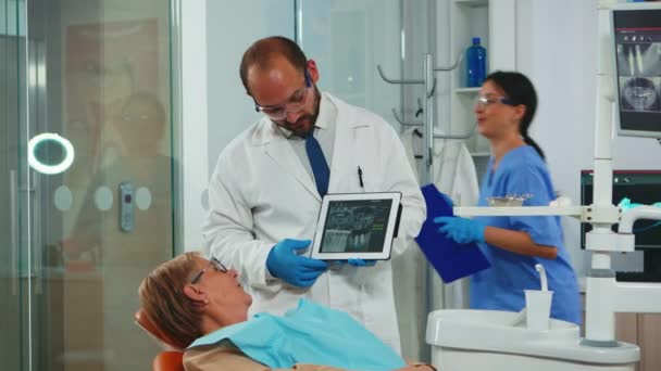 Ortodoncista usando tableta para explicar las radiografías dentales al paciente — Vídeos de Stock