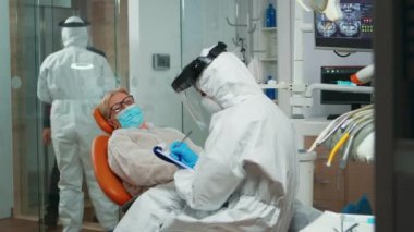 Koruyucu kıyafetli dişçi hemşire not alıyor.