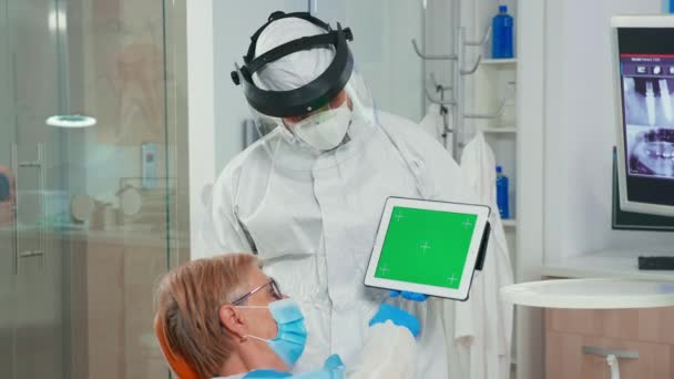 Dentista en mono apuntando a pantalla verde en unidad dental — Vídeo de stock