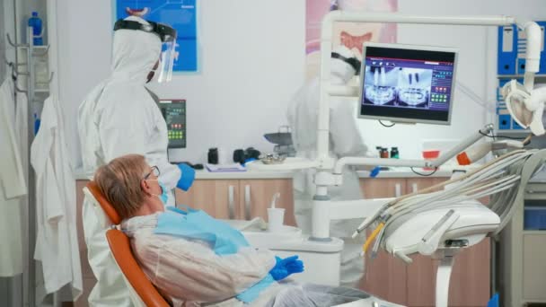 Estomatólogo en traje protector explicando radiografía dental — Vídeos de Stock