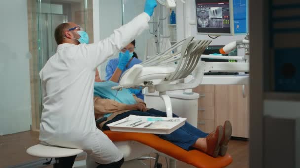 Dentista que trata os dentes para a paciente idosa na clínica — Vídeo de Stock