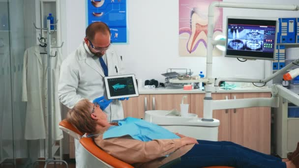 Kobieta siedząca na krześle dentystycznym słuchająca lekarza patrzącego na tabletkę — Wideo stockowe