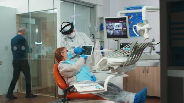Zubař v kombinéze zobrazující zubní rentgen tabletu — Stock video