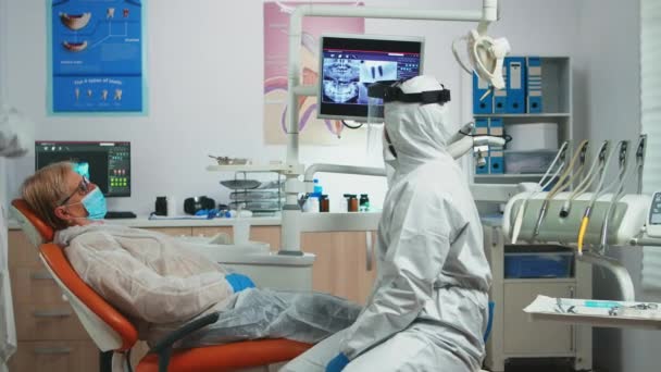 Médico dentista con equipo de protección que habla con el paciente viejo — Vídeos de Stock