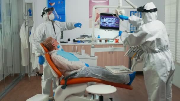 Стоматолог в защитном костюме осматривает зубы с помощью медицинских инструментов — стоковое видео