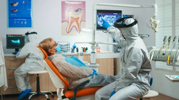 Dentista em terno de proteção explicando o processo de cirurgia dentária — Fotografia de Stock