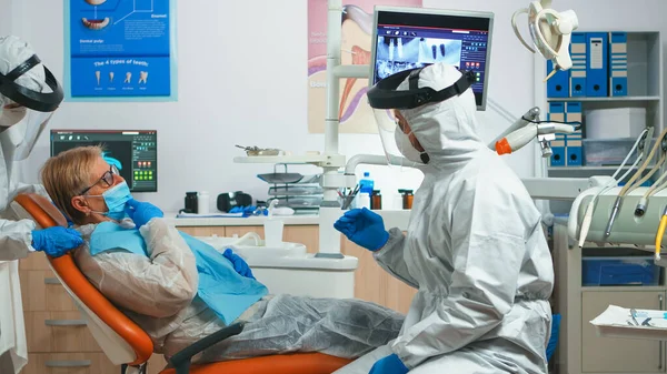 Médecin dentiste avec équipement de protection parlant avec un vieux patient — Photo