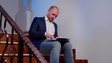 İşadamı merdivenlerde oturan belgeleri analiz ediyor.