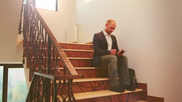 Бізнесмен, що друкує на смартфоні, сидить на сходах — стокове відео
