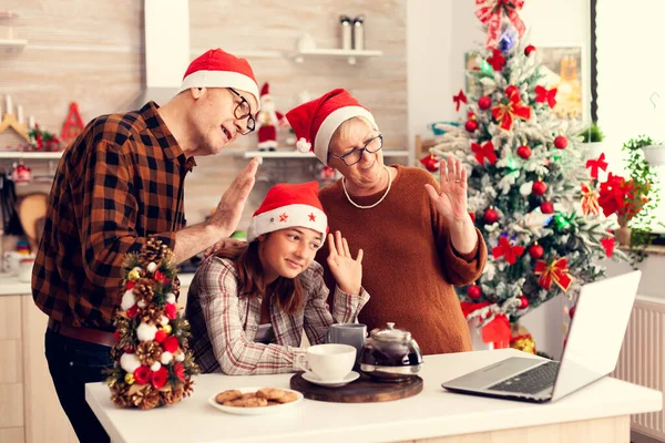 Grandparents celebrating christmas with niece in home waving at webcam talking with relatives.