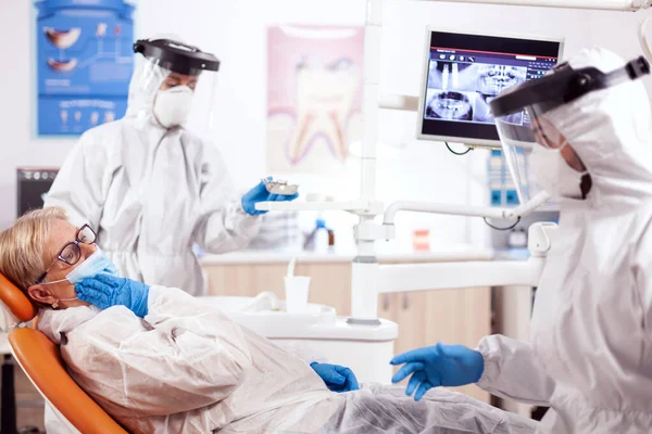 Старший пациент с болью в зубах надевает защитный костюм против коронавируса — стоковое фото