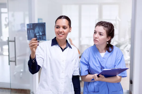 Dentist doctor holding teeth x-ray and nurse taking notes — Stock Photo, Image