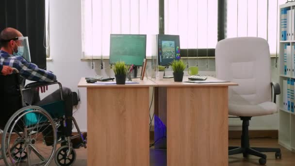 戴面具的同事帮助瘫痪的男人坐到办公桌前 — 图库视频影像