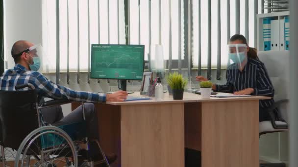 Biznesmen z maską poruszający się z wózkiem inwalidzkim w miejscu pracy — Wideo stockowe