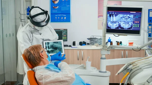 Médico en traje protector discutiendo sobre rayos X usando tableta —  Fotos de Stock