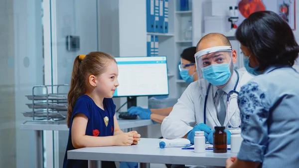 Dokter in gesprek met kind met beschermend masker — Stockfoto