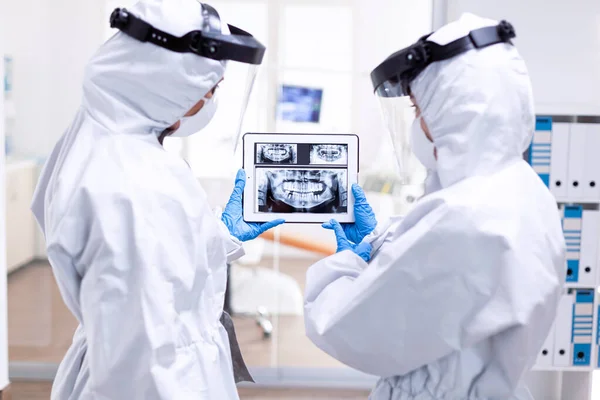 Médicos estresados vestidos con traje de protección mirando rayos X dentales digitales — Foto de Stock