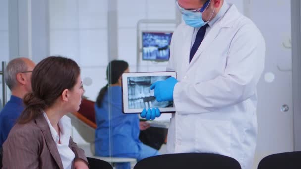 Femme assise sur la chaise écoutant médecin regardant sur tablette avec rayons X — Video