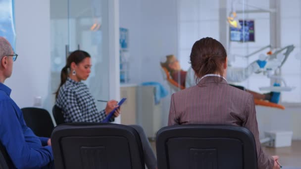 Vista posterior del paciente llenando el formulario dental sentado en el chiar — Vídeos de Stock