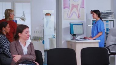 Diş hekimi resepsiyonda yaşlı bir kadınla konuşuyor.