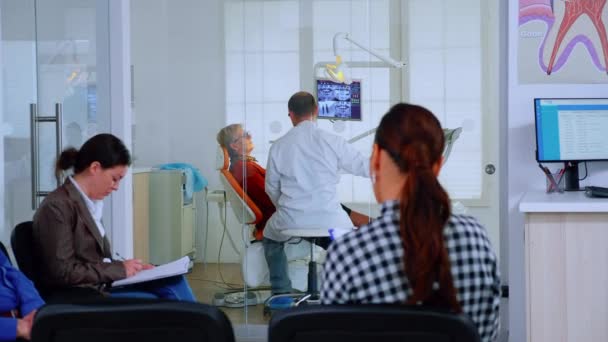 Пациенты, сидящие на стульях в приемной стоматологической клиники — стоковое видео