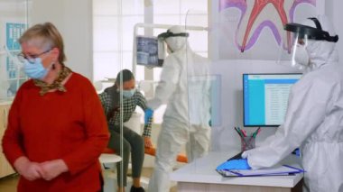 Koruyucu kıyafetli doktor, dişçi odasına bir sonraki hastayı davet ediyor.