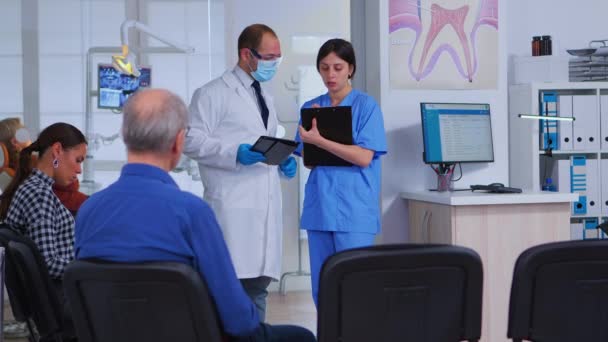 Стоматолог разговаривает с ассистентом, стоящим в приемной — стоковое видео