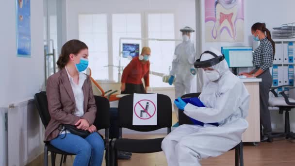 Медсестра-стоматолог с защитным оборудованием разговаривает с пациентом — стоковое видео