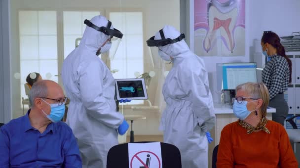 Man discussing with nurse in dental reception wearing protection suit — Stock Video