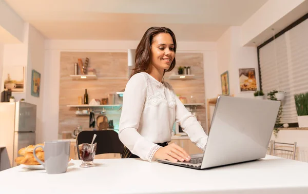 Empresária fazendo horas extras trabalhando no laptop na cozinha doméstica — Fotografia de Stock