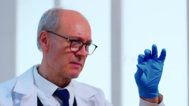 Старий вчений аналізує зразок вірусу в сучасній лабораторії — стокове відео