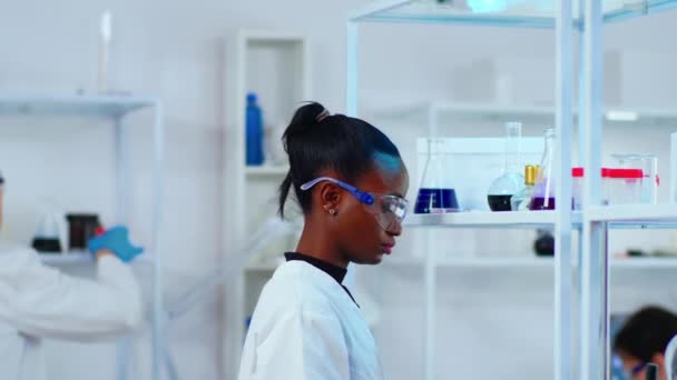 Femeie africană cercetător chimist folosind echipamente de sticlă în laborator — Videoclip de stoc