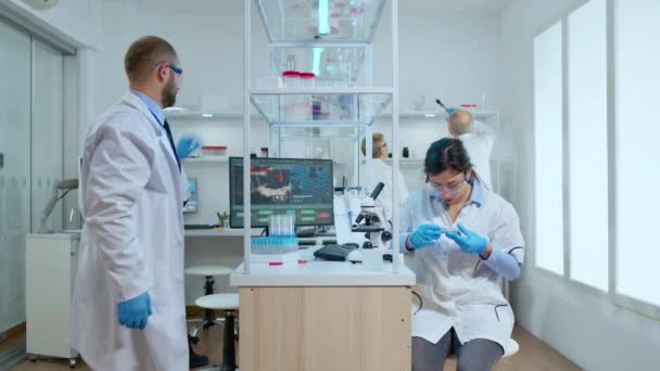 Mujer científica examinando placa de Petri y mirando hacia abajo en el microscopio — Vídeos de Stock