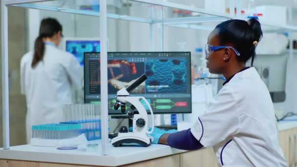 Černá biochemička žena sedí v laboratoři a analyzuje krevní testy — Stock video