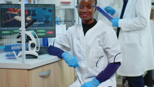 Μαύρη γιατρός γυναίκα χαμογελά στην κάμερα κάθεται σε επιστημονικό εργαστήριο — Αρχείο Βίντεο