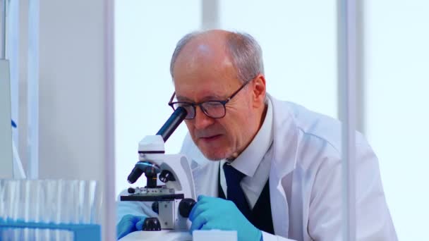 Senior laboratoriumtechnicus die monsters en vloeistof onderzoekt met behulp van microscoop — Stockvideo