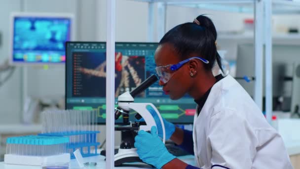 Biochimico donna africana utilizzando il microscopio in laboratorio — Video Stock